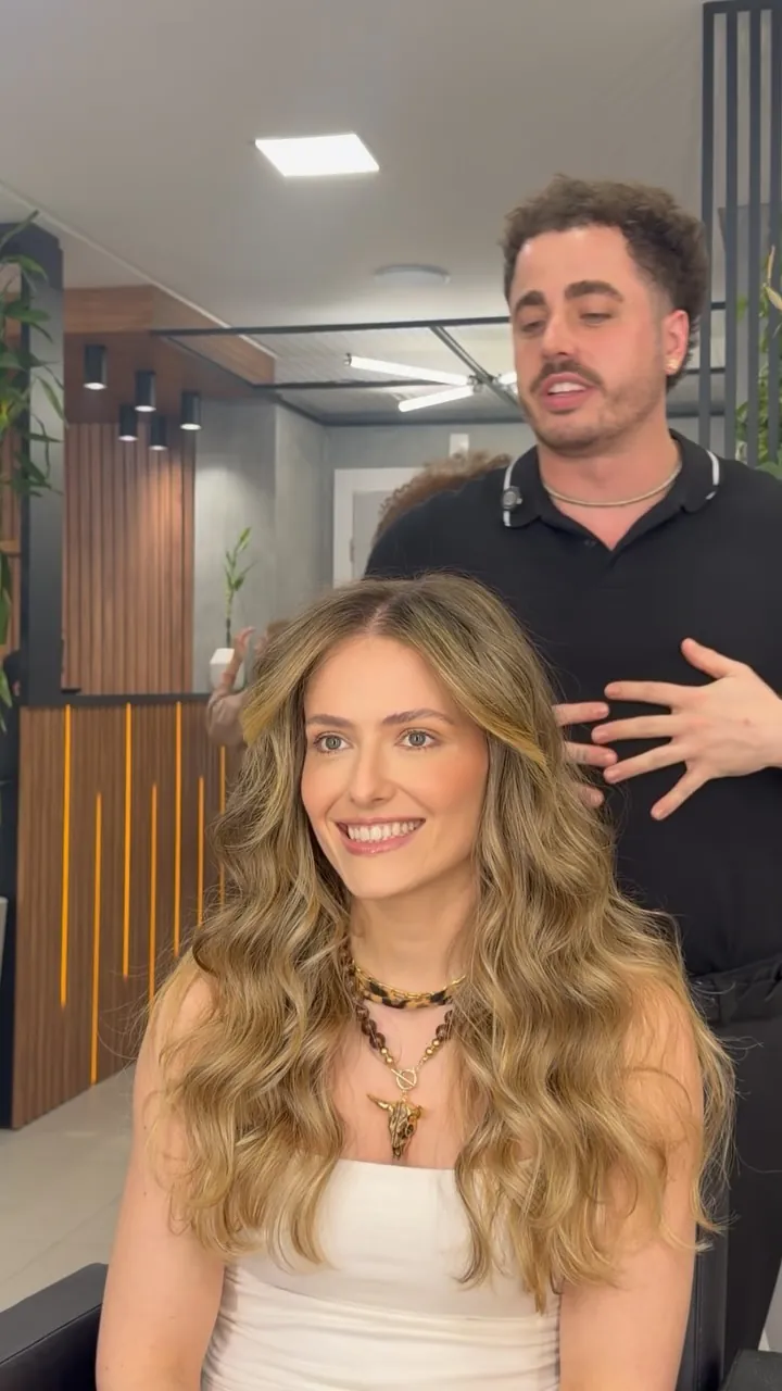 Cliente com ondas loiras ao lado do cabeleireiro no salão